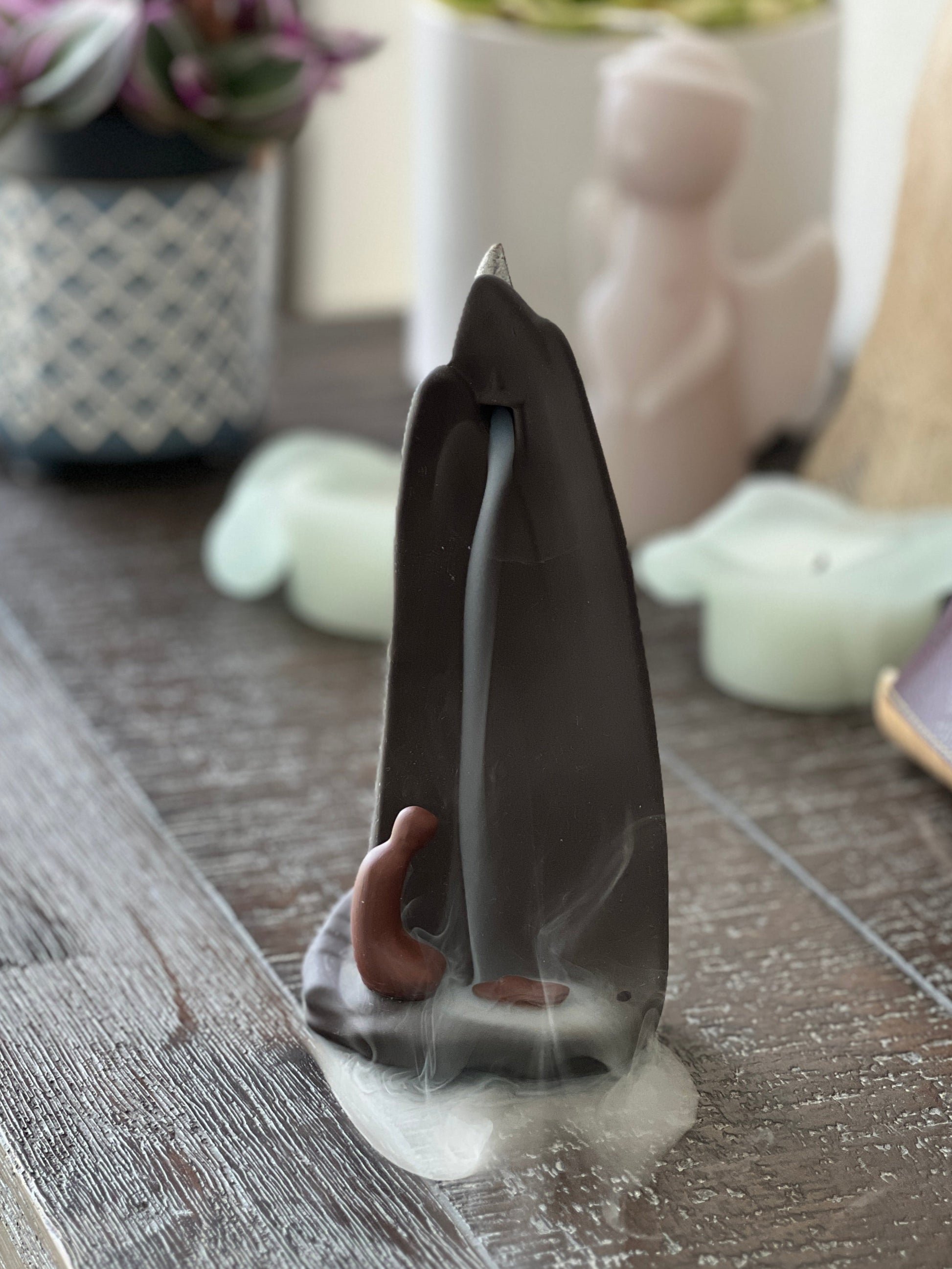 Incense burner with smoke on a wooden surface with decorative items in the background